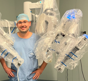 Dr. Thiago Teixeira ao lado do sistema robótico de cirurgia minimamente invasiva em centro cirúrgico.