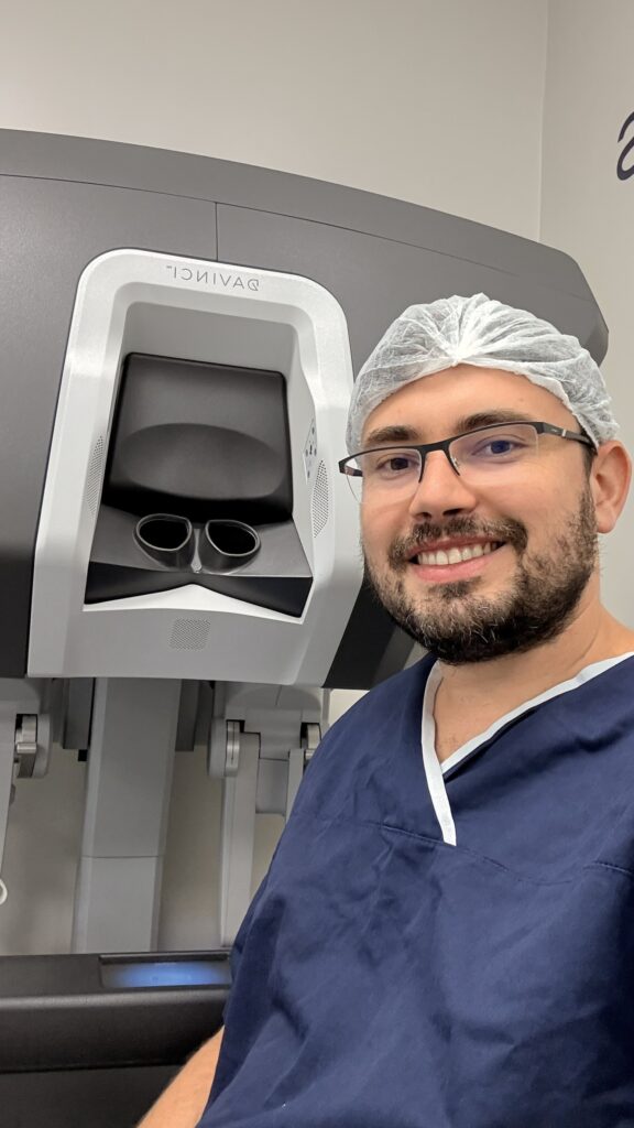 Dr. Thiago Teixeira, urologista especialista em cirurgia robótica, ao lado do robô cirúrgico Da Vinci utilizado em procedimentos minimamente invasivos.