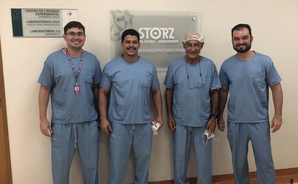 Dr. Thiago Teixeira ao lado do Dr. Mirandolino de Carvalho, pioneiro da laparoscopia da próstata, em centro de treinamento cirúrgico.